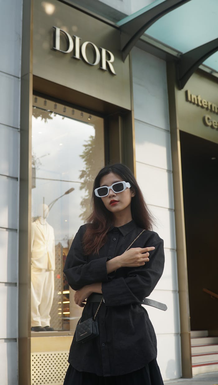 Fashionable woman with sunglasses posing stylishly outside a Dior store.