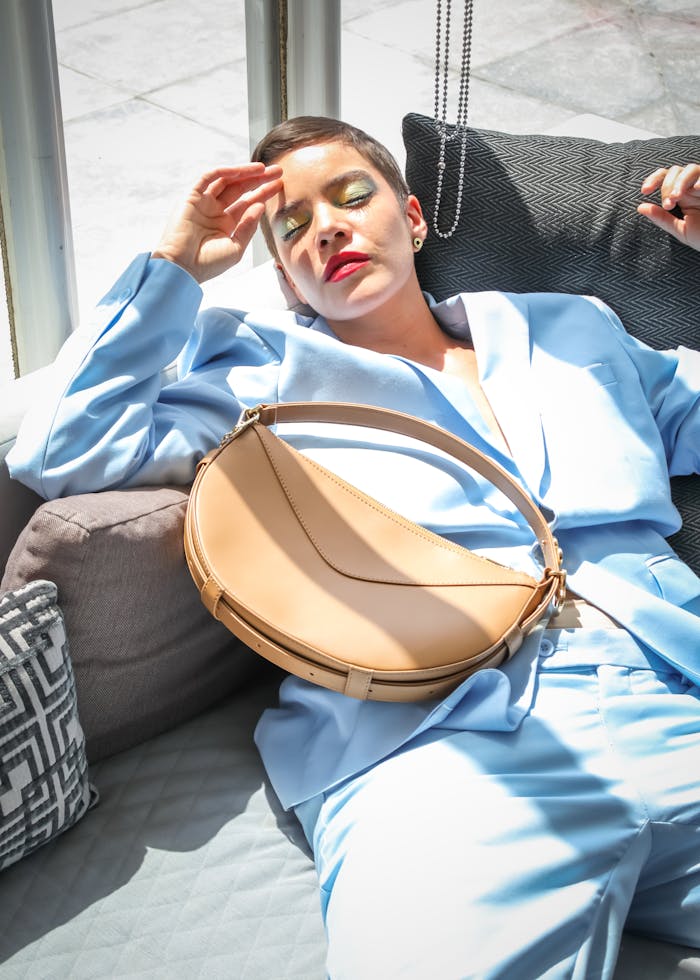 A fashionable woman in a blue suit relaxes indoors, showcasing modern style and elegance.